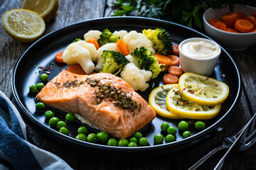 Steamed salmon steak with cauliflower, broccoli, carrots, lemon, peas and mayonnaise on wooden table 
