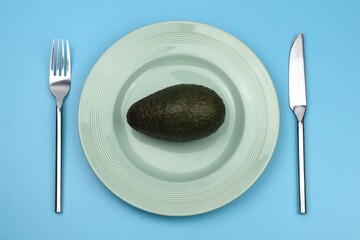 avocado in a plate with knife and fork on blue background 
