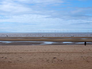the beach at blundel sands in southport with water on the beach and the wind turbines at burbo bank visible in the distance