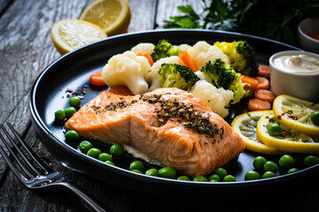 Steamed salmon steak with cauliflower, broccoli, carrots, lemon, peas and mayonnaise on wooden table 
