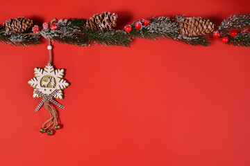 Christmas toy in the form of snowflakes, with a deer and bells, hanging on a spruce branch, on a red background. New year's snowflake. Wooden decoration for Christmas tree