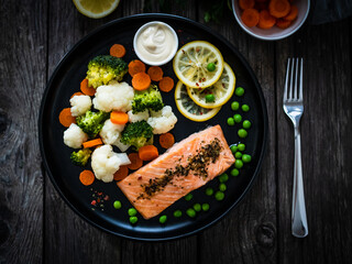 Steamed salmon steak with cauliflower, broccoli, carrots, lemon, peas and mayonnaise on wooden...