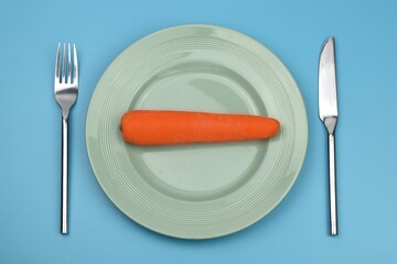  carrot in a plate with knife and fork on blue background 