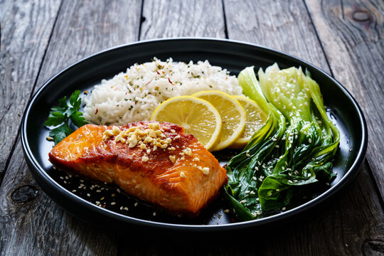 Fried salmon steak with lemon, basmati rice and steamed pak choi cabbage served on wooden table
