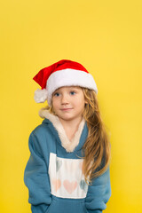 Little beautiful girl in santa hat smiling isolated on yellow background