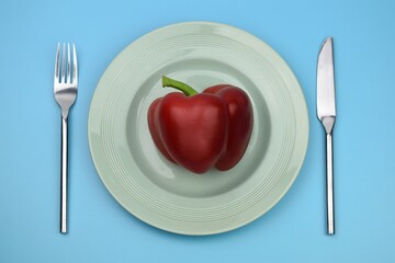 red pepper bell on a plate with knife and fork on a blue background 