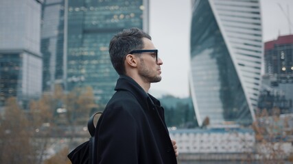 Man in black coat walk on background of business skyscrapers, slow motion. Gimbal profile shot of...