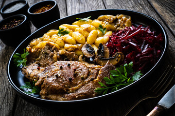 Roasted pork steaks, noodles and pickled beetroot and onion on wooden table

