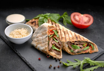 Shawarma with meat, cutaway, with sauce, tomatoes, cheese, herbs and garlic, on black slate, on a black background