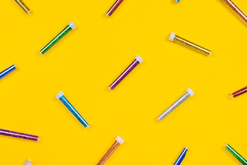 Jars of colorful glitter isolated on yellow background. Flat lay pattern