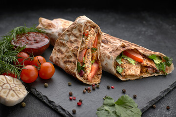Shawarma with meat, cutaway, with sauce, tomatoes, cheese, herbs and garlic, on black slate, on a...