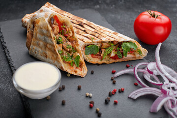 Shawarma with meat, cutaway, with sauce, tomatoes, cheese, herbs and garlic, on black slate, on a black background