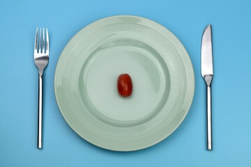 cherry tomato on a plate with knife and fork on blue background 