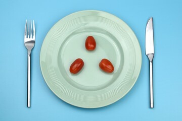 cherry tomatoes on a plate with knife and fork on blue background 