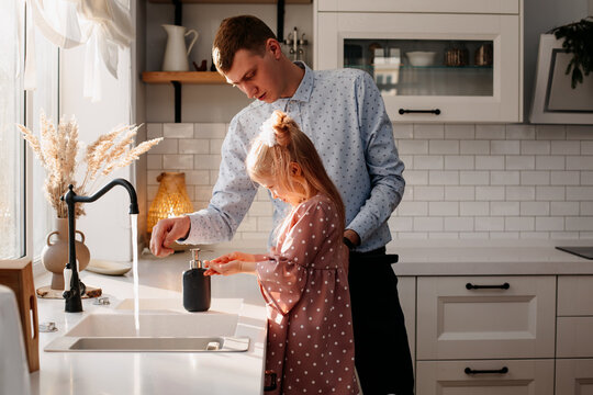 little girl washes her hands with water in the kitchen, next to her father. cleanliness and health concept
