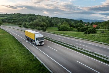 Truck with semi-trailer driving along highway on the sunset background. Goods delivery by roads. Services and Transport logistics