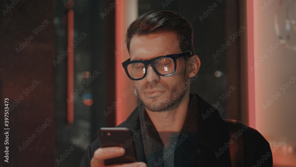 Poster man in eyeglasses with phone in hand on background of building with lights on. handheld night shot o