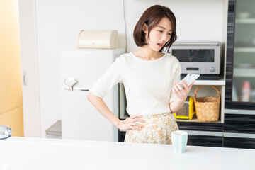 キッチンでスマホを見る女性　考える