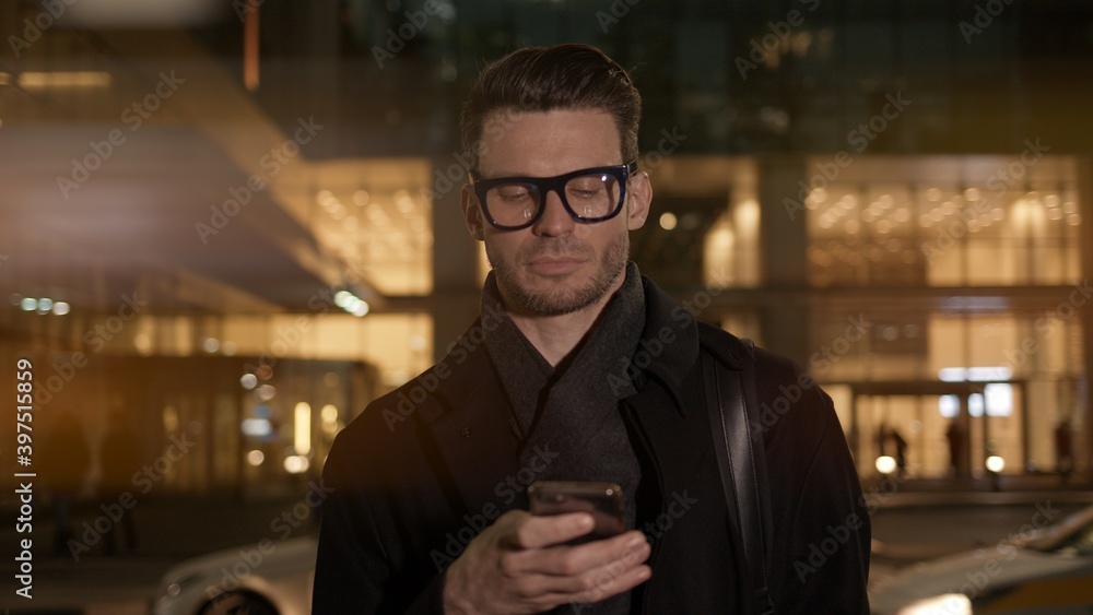 Fototapete man in eyeglasses with phone in hand on background of building with lights on. gimbal night shot of 