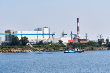industrial landscape with a factory on the banks of the river, along which a motorship floats