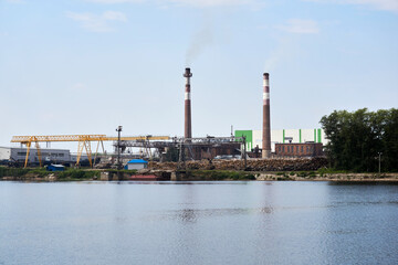 Fototapeta na wymiar industrial landscape, pulp and paper mill with stacks of logs on the river bank