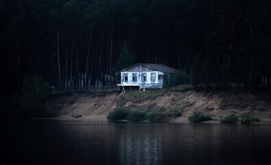 abandoned dilapidated house on a dark wooded bank almost collapsed into the river