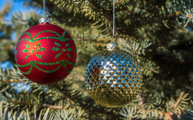 Fototapeta na wymiar Two colorful Christmas ornaments hanging on the branches of a pine tree outdoors with copy space