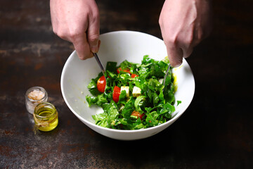 Salad in a white bowl mixed by the hands of the cook. Cooking a healthy salad. Fitness food. Healthly food.