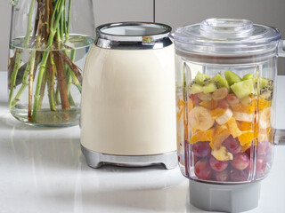 Prepared smoothies and healthy smoothie ingredients in blender with fresh fruit ready to blend on kitchen table