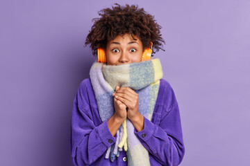 Afro American woman feels very cold during freezing weather wears purple jacket and warm scarf...