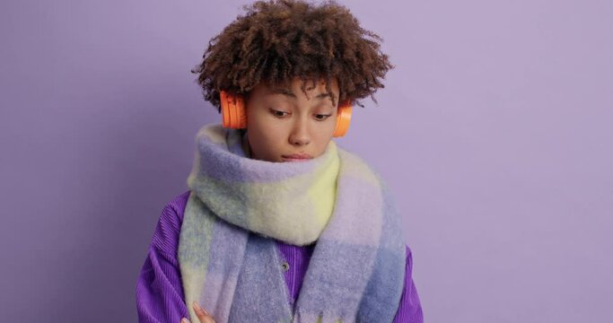 Pensive hesitant young woman shakes head and cannot decide what answer to give stands uncertain gets proposal to have walk during winter dressed in purple jacket and scarf around poses alone