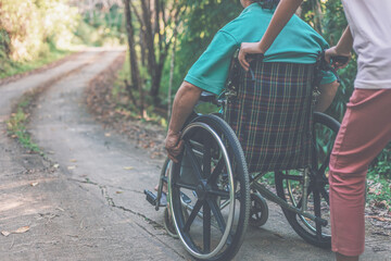Naklejka premium disabled handicapped man in wheelchair and care helper walking in park.