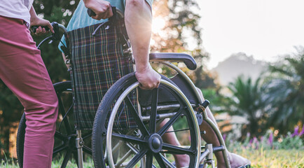 disabled handicapped man in wheelchair and care helper walking in park.
