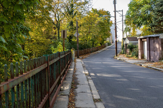 Street and narrow sidewalk bordered by a rusted cast iron fence, garages, early fall urban landscape, horizontal aspect