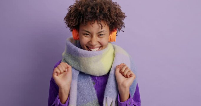 Ethnic girl eager to hear something very pleasant clenches fists and closes eyes with anticipation wears warm clothes isolated over purple studio background. People and positive emotions concept