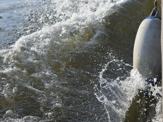 Rushing water quickly bursts out from under the bow of the boat, flowing around the fender