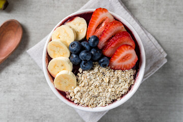 Brazilian frozen açai berry ice cream bowl with strawberries, bananas, blueberry and oatmeal flakes. with fruits on wooden background. Summer menu top view. close up