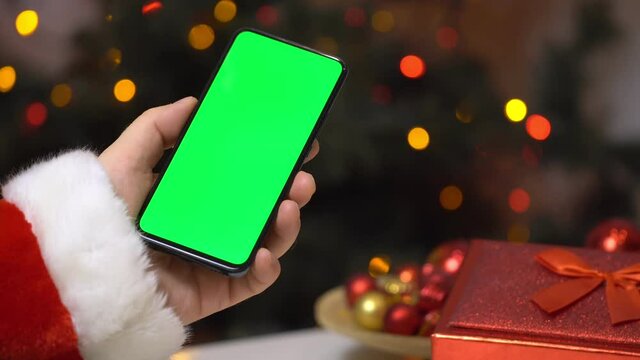 Close up shot of male in santa claus clothes at night, holding a smartphone with chroma key mock up green screen - technology, connections, communications concept 4k video template