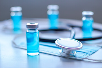 Vaccines Vials with a stethoscope and a face mask on a white table.