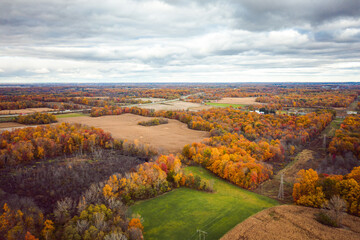 Beautiful aerial photograph of green and golden farm fields in Indiana in Fall with colorful red, yellow and orange autumn foliage or leaves on the forests of trees scattered across the landscape.