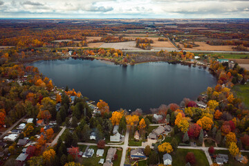 Beautiful full aerial view of the heart shaped Saugany Lake in Indiana surrounded by residential homes and autumn colored trees or foliage with fluffy white clouds in the sky above.