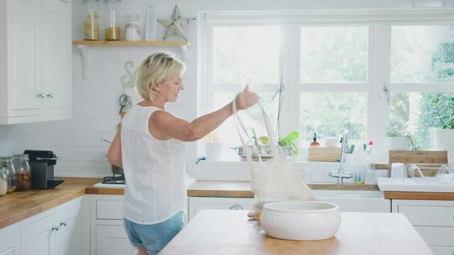 Retired senior woman unpacking local food in zero waste packaging from bag in kitchen at home - shot in slow motion