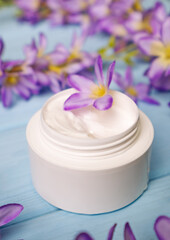 Fototapeta na wymiar Natural cosmetic body care cream on a background of blooming purple flowers on a wooden blue background. Moisturizing cosmetic cream, skin care natural cosmetics.