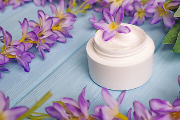 Natural cosmetic body care cream on a background of blooming purple flowers on a wooden blue background. Moisturizing cosmetic cream, skin care natural cosmetics.