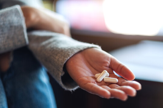 Closeup image of a woman holding white medicine capsules in hand