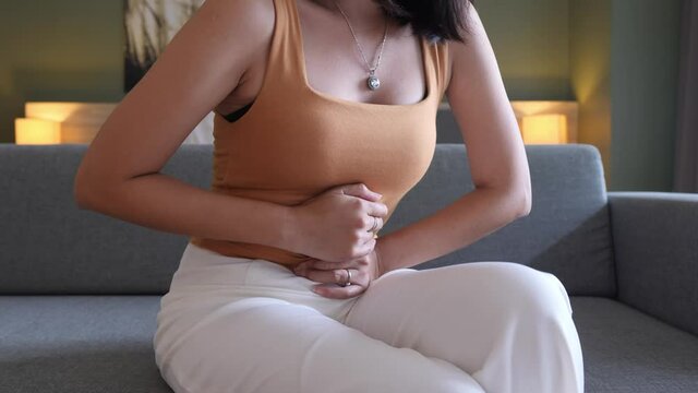 Women having painful stomach ache sitting on sofa,Female suffering from abdominal pain,Period cramps,Hands squeezing belly,Stomach pain,Menstruation