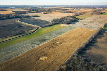 Fototapeta premium Beautiful autumn aerial of a drainage ditch or creek running through farm fields in rural Wisconsin with patches of trees, farms, barns, and silos spread throughout the landscape beyond on a sunny day