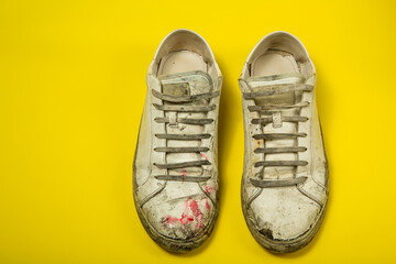 Dirty shoes, vintage white torn sneakers isolated on a yellow background.