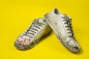Dirty shoes, vintage white torn sneakers isolated on a yellow background.