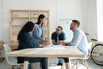 Concentrated diverse young businesspeople engaged in team discussion at business meeting in office. Multiracial employees colleagues talk brainstorm think together at briefing. Teamwork concept.